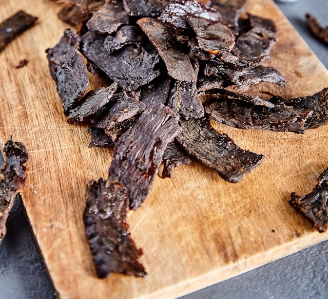 A pile of beef jerky laying on a wooden cutting board